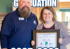 The President and CEO of the Austin Area Chamber of Commerce standing next to a Leadership Austin cohort student, Anna Good, at the graduation ceremony while holding a certificate of achievement.